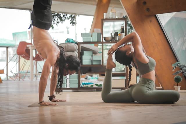 Woman gracefully performing a deep stretch while a man expertly maintains a handstand beside her, illustrating the pillars of Flexibility, Agility, and Balance