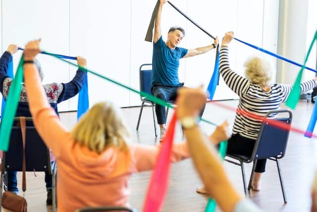 Elderly individuals seated in chairs, using resistance bands for exercise, highlighting 'Fitness for Different Age Groups