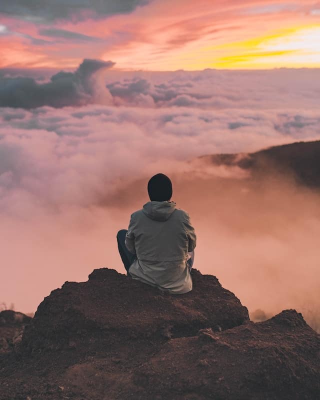 Man meditating serenely on a mountain peak, elevated above a sea of clouds, embodying the essence of Mindfulness in Motion